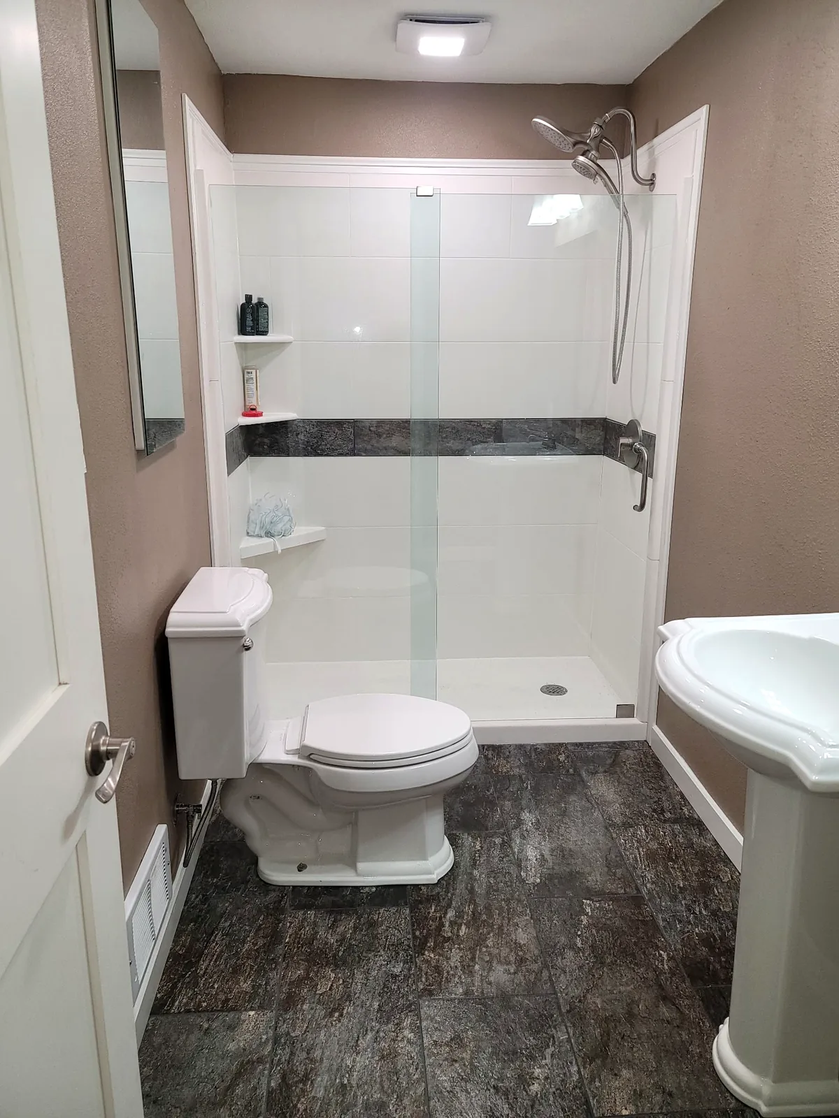 Walk-in shower with glass panel, tile accent band, and dark stone-look floor